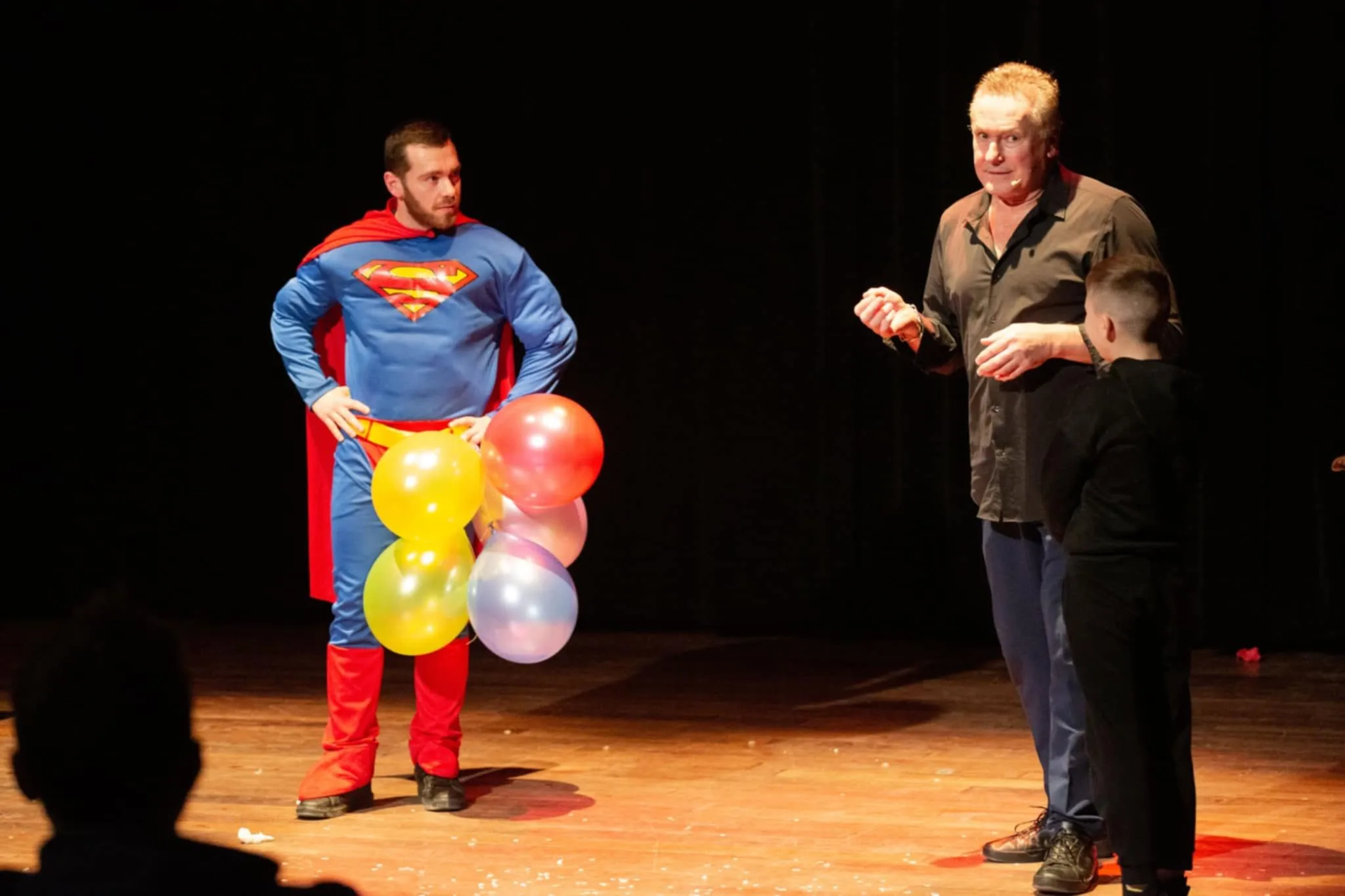 Participation du public : un spectateur déguisé en super-héros avec des ballons, aux côtés de Mickaël Ross