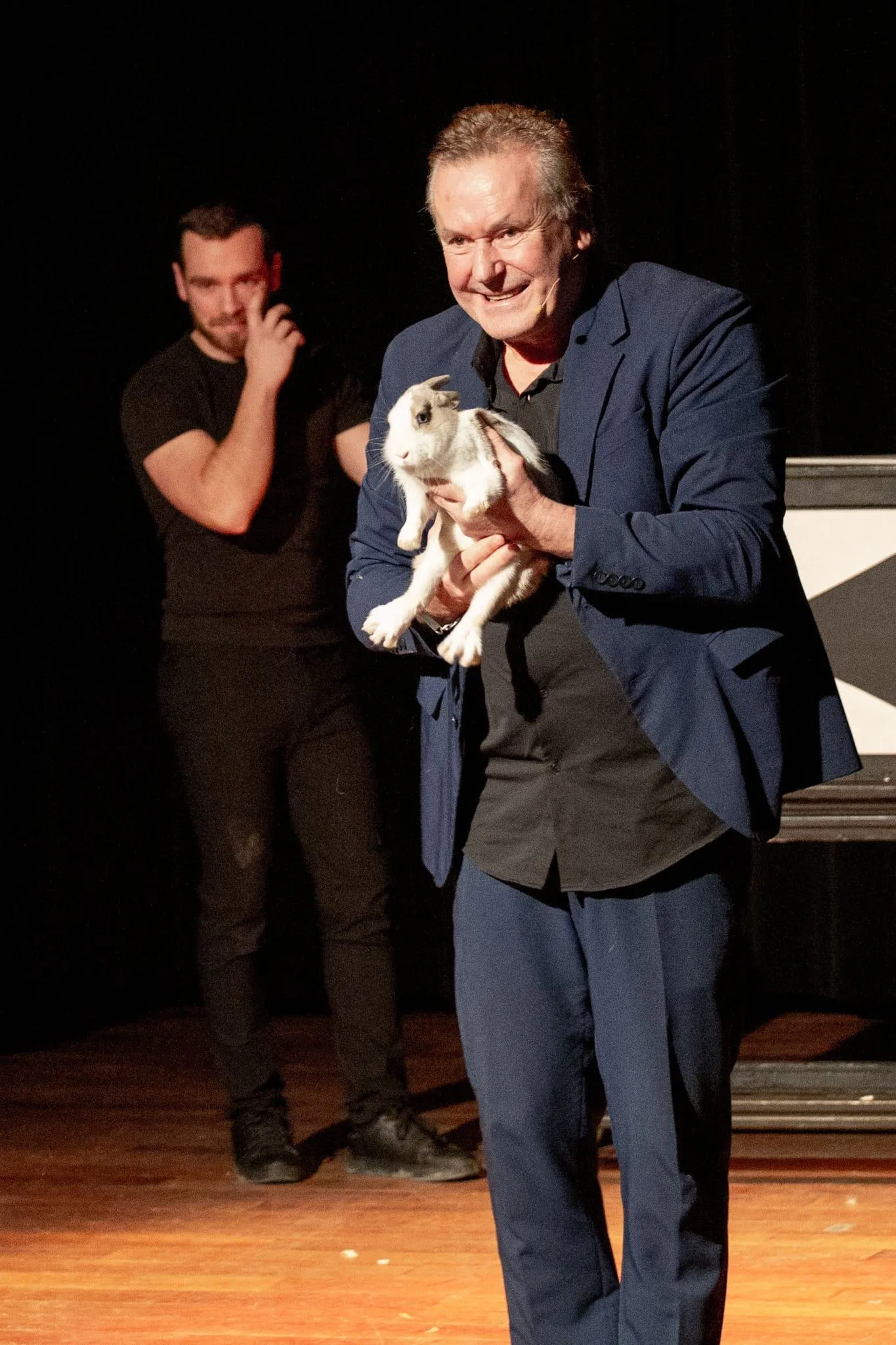 Mickaël Ross sur scène tenant un lapin blanc pendant son spectacle