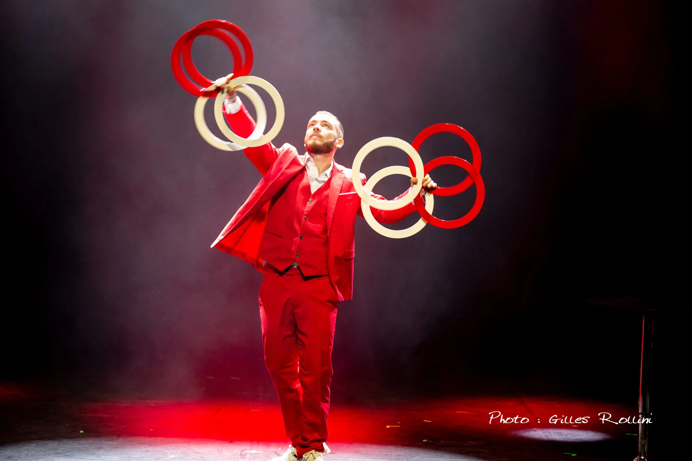 Jongleur en costume rouge lançant des anneaux rouges et blancs sous les projecteurs